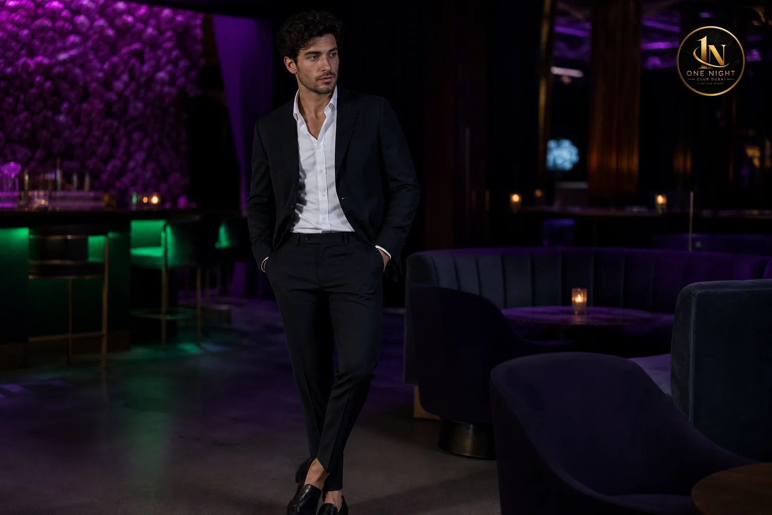 Photorealistic photograph of a stylish man in his late 20s wearing a fitted black blazer over a crisp collared shirt, dark tailored trousers, and polished leather loafers, standing in a dim upscale nightclub lounge with purple and green